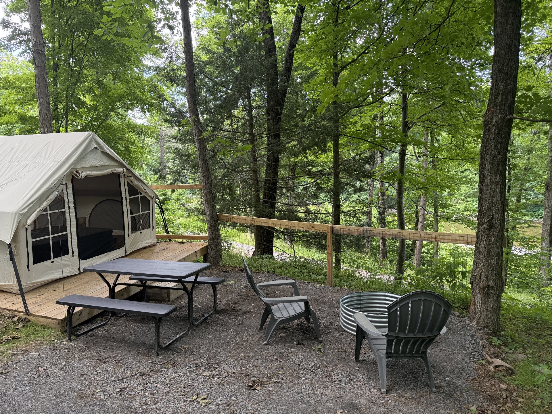Beige canvas tent on a wooden deck in a forest, with a black picnic table and benches nearby.