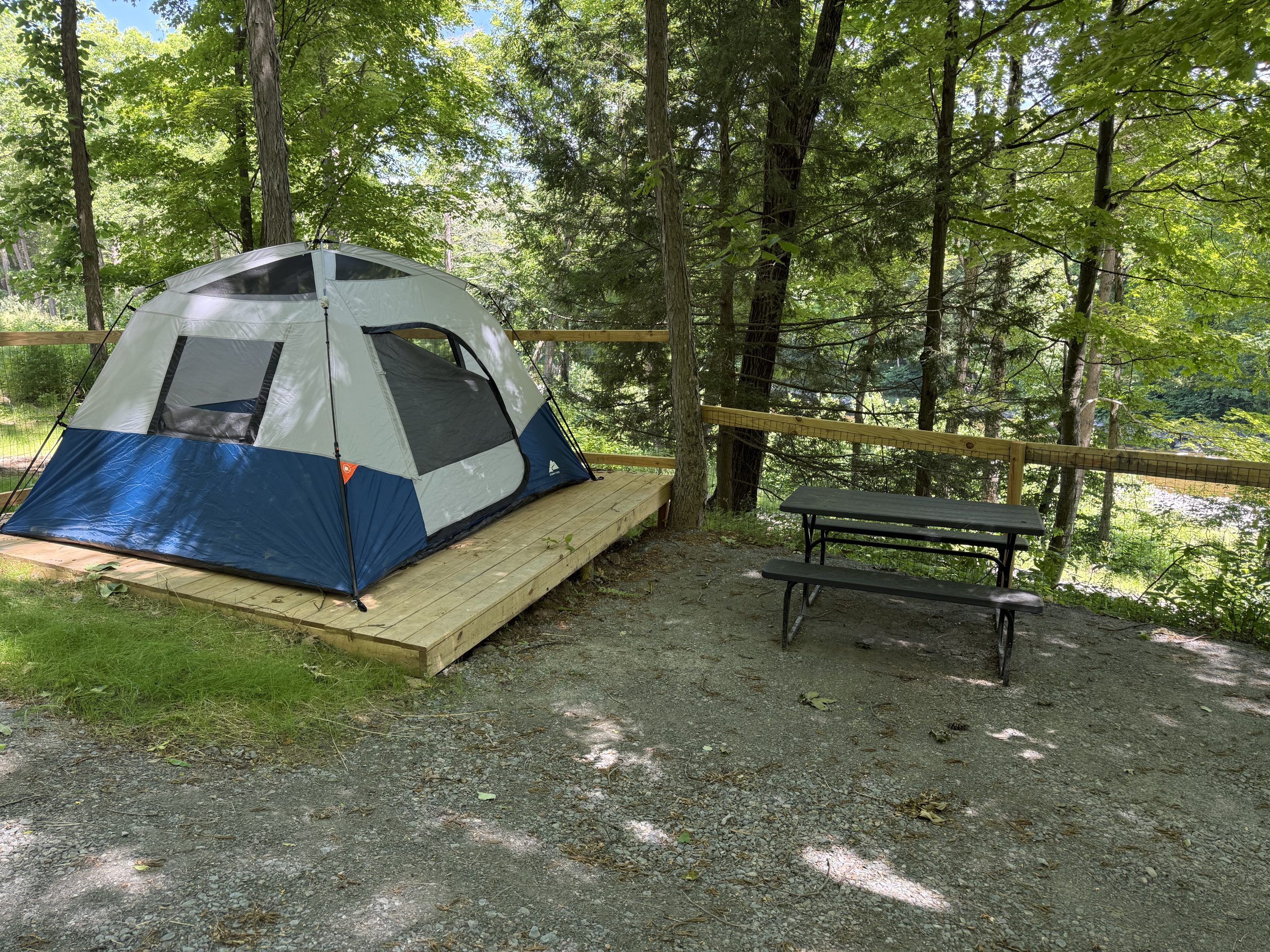 Tented campsite on a wooden platform amid green trees, with a picnic table nearby.